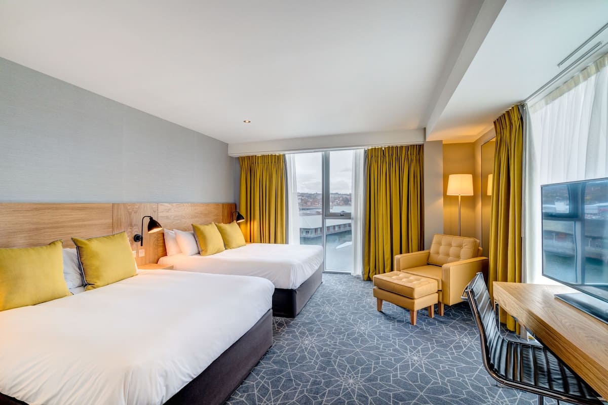 A hotel room with two beds, a desk, a chair, and a large window with curtains.