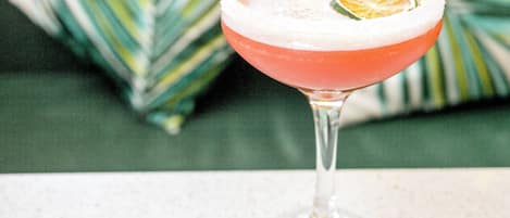A cocktail in a stemmed glass with a salted rim, garnished with a slice of lime, on a speckled countertop.