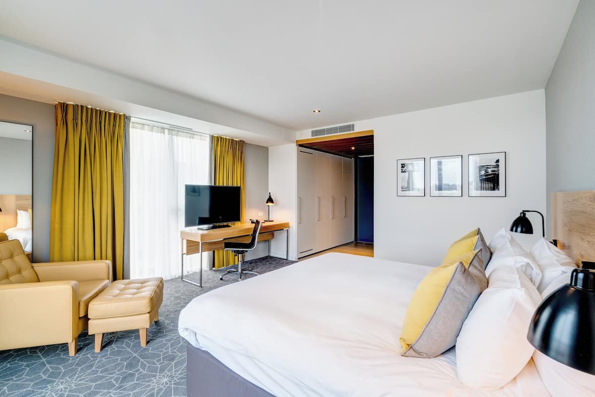 A hotel room with a bed, a desk, a chair, a television, and a wardrobe.