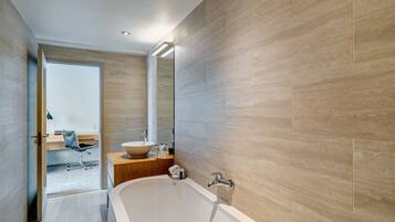 A modern bathroom with a freestanding bathtub, a vanity with a bowl sink, and a mirror above the sink.