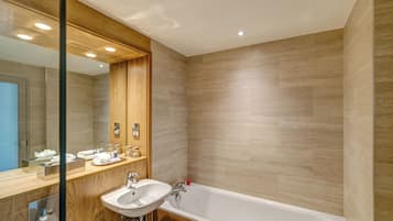 A modern bathroom with a wooden vanity, a large mirror, a white sink, and a bathtub.