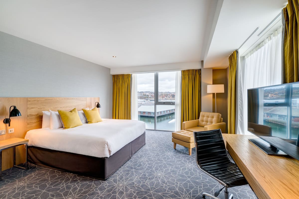 A modern hotel room with a large bed, a desk, a chair, and a TV.
