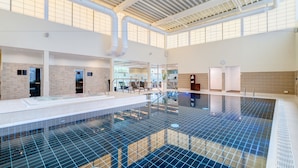 A large indoor swimming pool with a tiled floor, a high ceiling with visible ductwork, and a seating area with chairs and a table. - Apex City Quay Hotel & Spa (Dundee)
