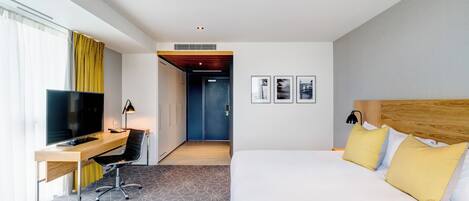Habitación de hotel con una cama, un escritorio con ordenador, una televisión y una silla.