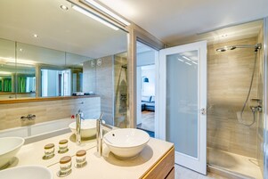 A modern bathroom with a large mirror, a bathtub, a shower, and a vanity with a sink and multiple jars.