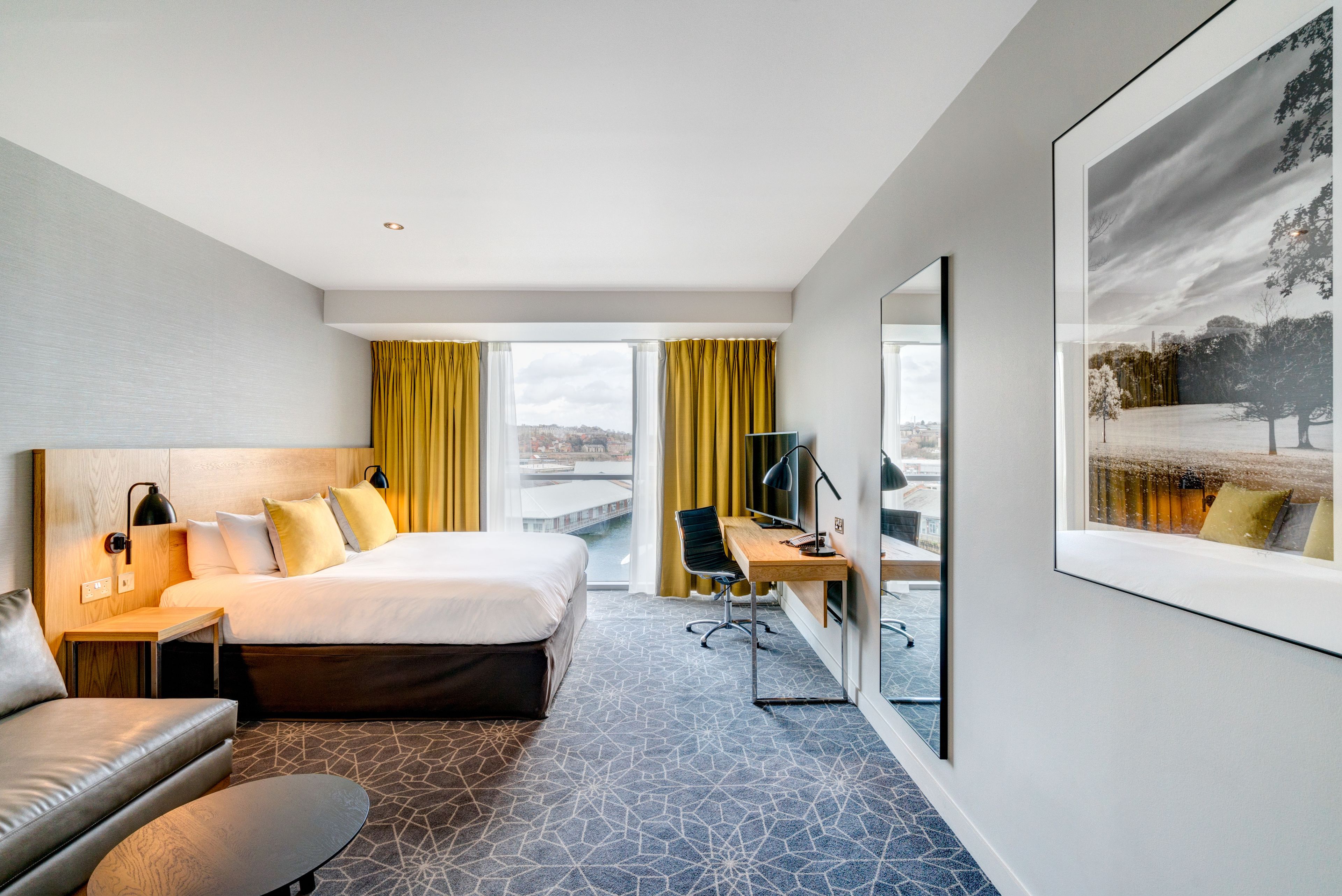 A modern hotel room with a large bed, a desk, and a view of the city.