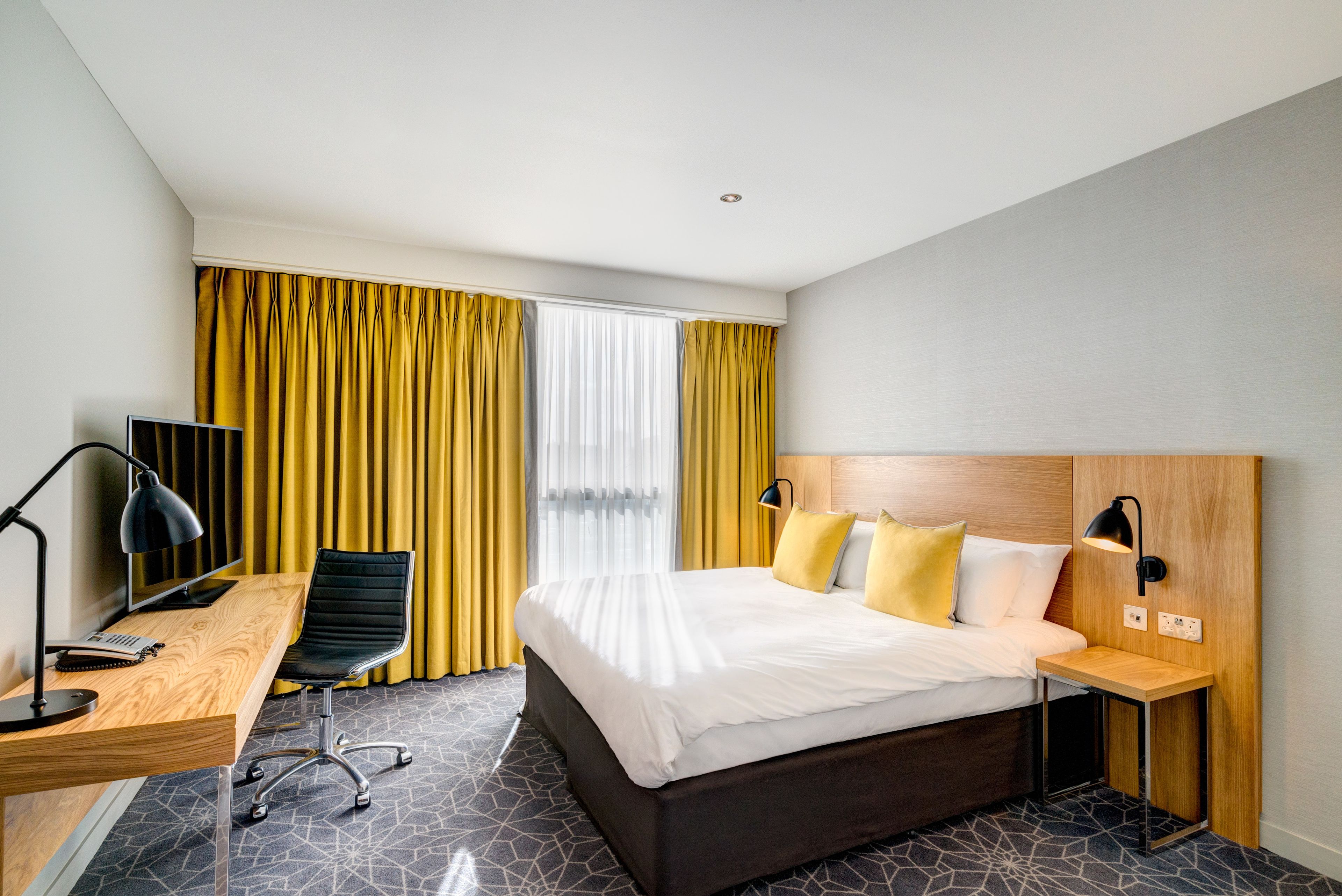 A hotel room with a bed, desk, chair, and a TV.