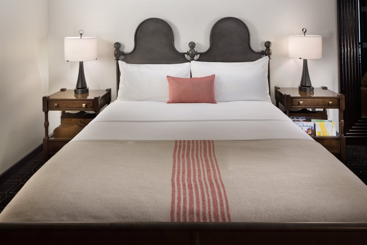 Een keurig opgemaakt bed met een rood-wit gestreepte lakensprei, twee bedlampjes en een donker hoofdbord.