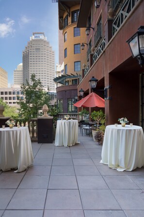 An outdoor patio area with tables set up for dining, surrounded by buildings and a clear sky. - Hotel Valencia Riverwalk (San Antonio)