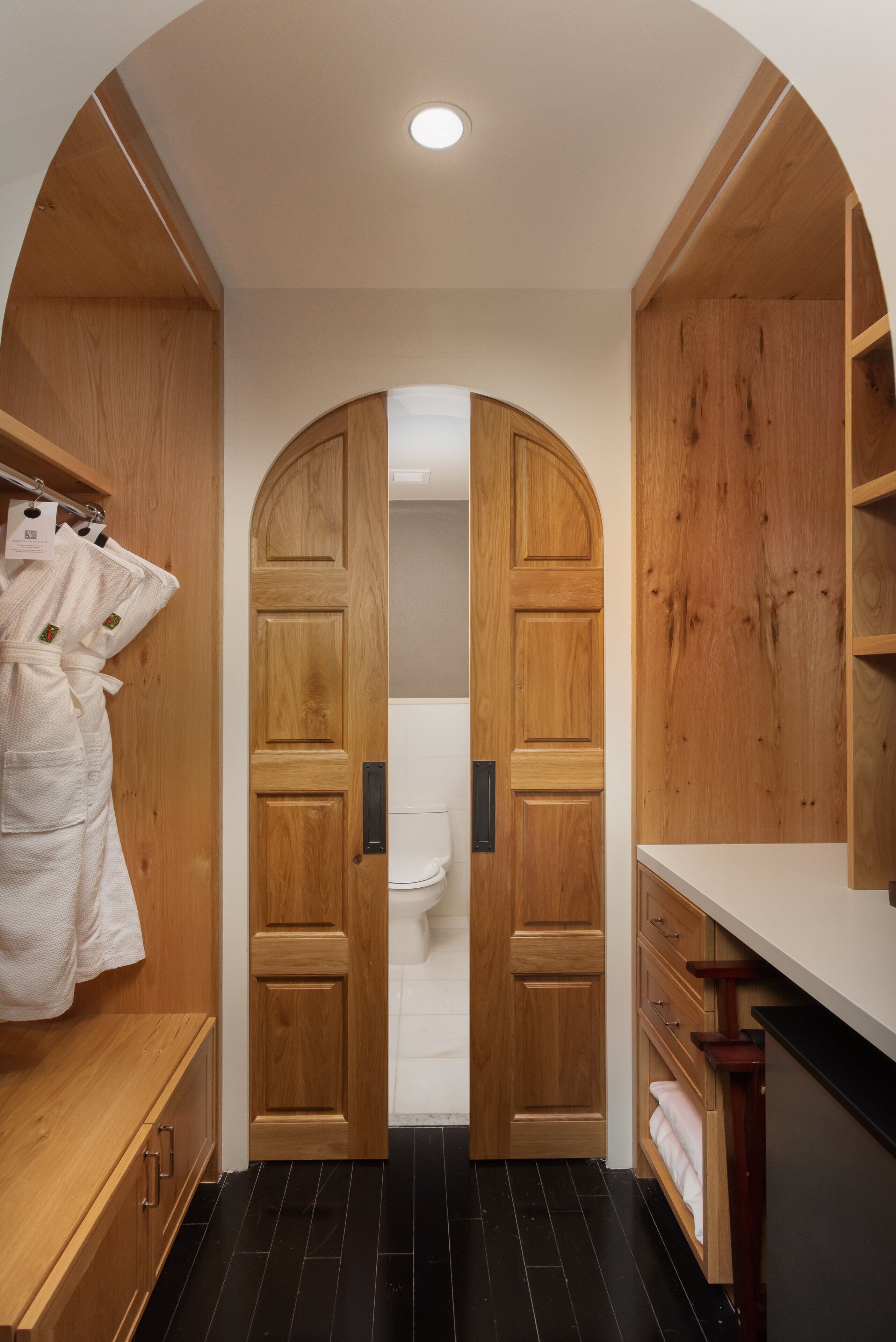 A wooden bathroom with a white toilet, a wooden vanity, and a robe hanging on a rack.