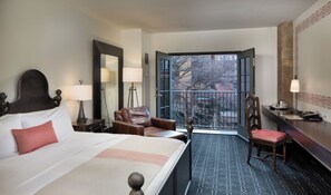 A hotel room with a bed, a desk, a chair, and a balcony with a view of trees and buildings. - Hotel Valencia Riverwalk (San Antonio)