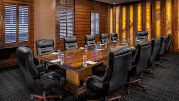 A conference room with a large wooden table, black leather chairs, and wooden paneled walls.