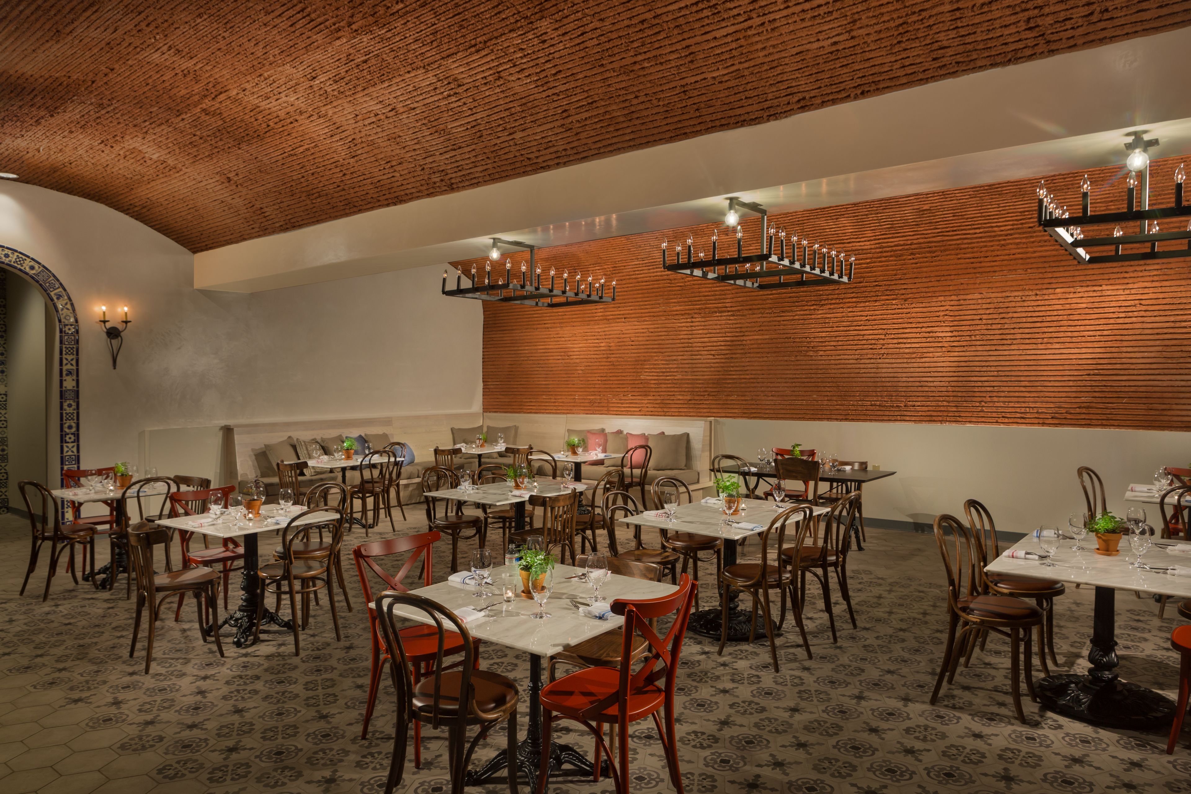 A spacious dining area with multiple tables and chairs, featuring a brick ceiling and wooden wall paneling.