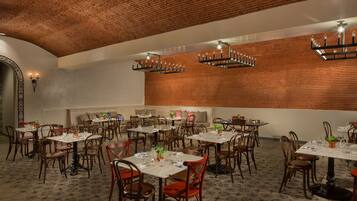 A spacious dining area with multiple tables and chairs, featuring a brick ceiling and wooden wall paneling.
