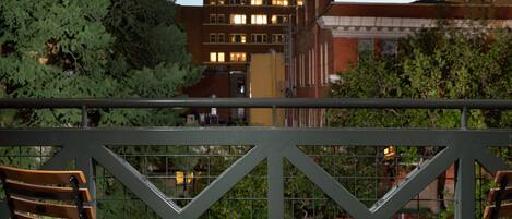 Een balkon met twee houten stoelen en een klein tafeltje, met uitzicht op een stadsgezicht met gebouwen en bomen.