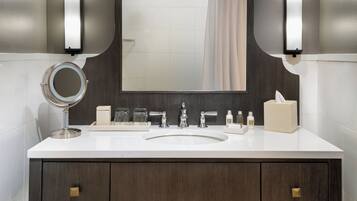 A modern bathroom with a large mirror, two wall-mounted lights, a white sink, and a dark wooden vanity.