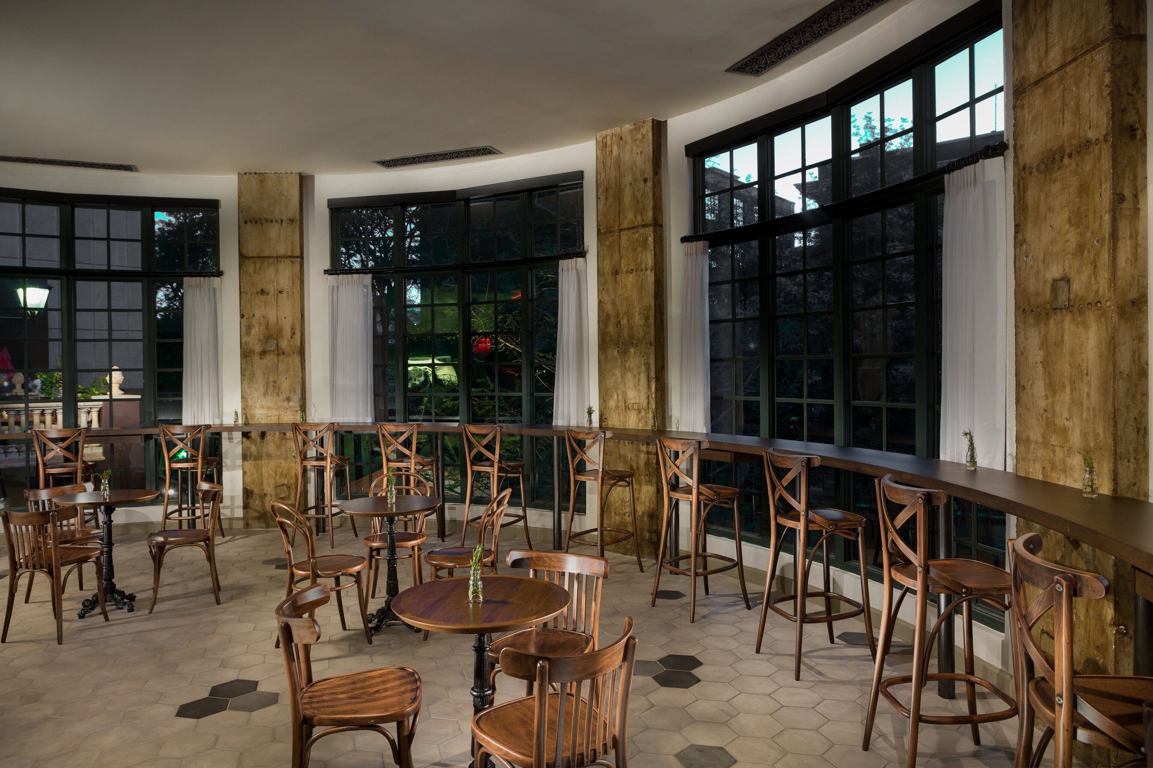 A spacious indoor dining area with wooden tables and chairs, large windows, and a view of the outdoors.