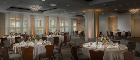 Ein Bankettsaal mit runden Tischen, gedeckt für ein Essen, mit weißen Tischdecken und Blumendekorationen in der Mitte.
