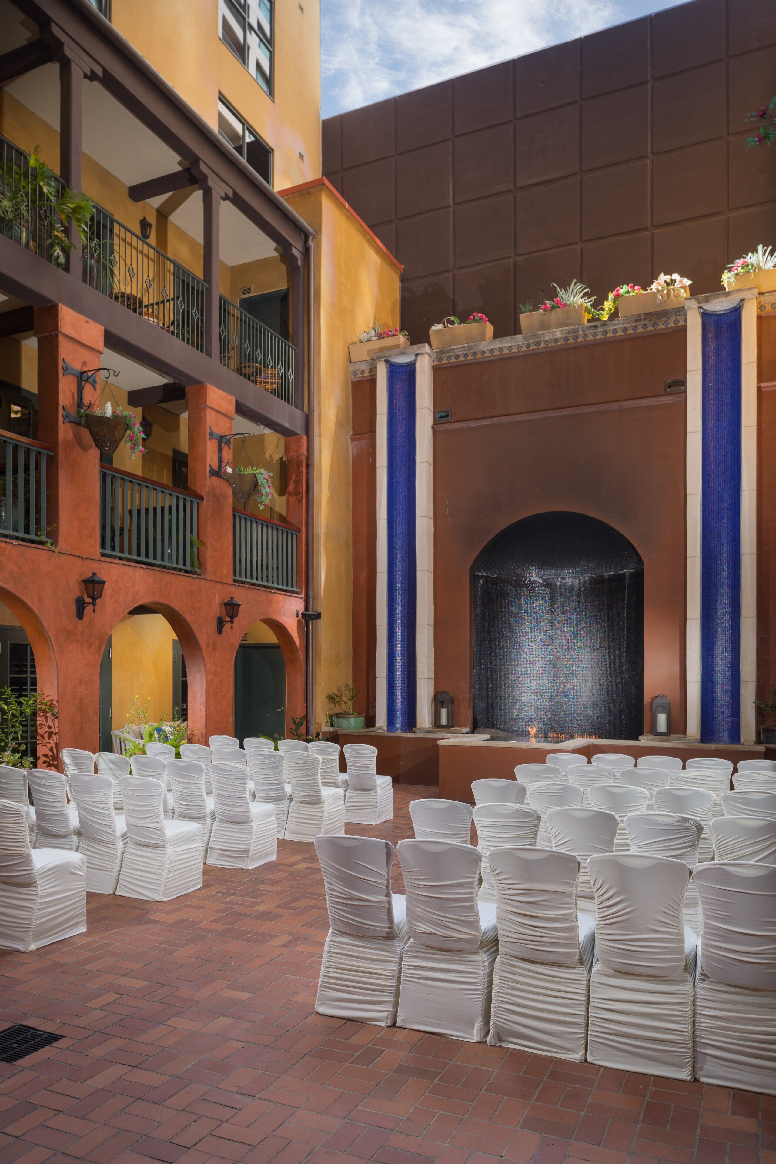 A courtyard with rows of white chairs, a central fountain, and a building with balconies and arches.