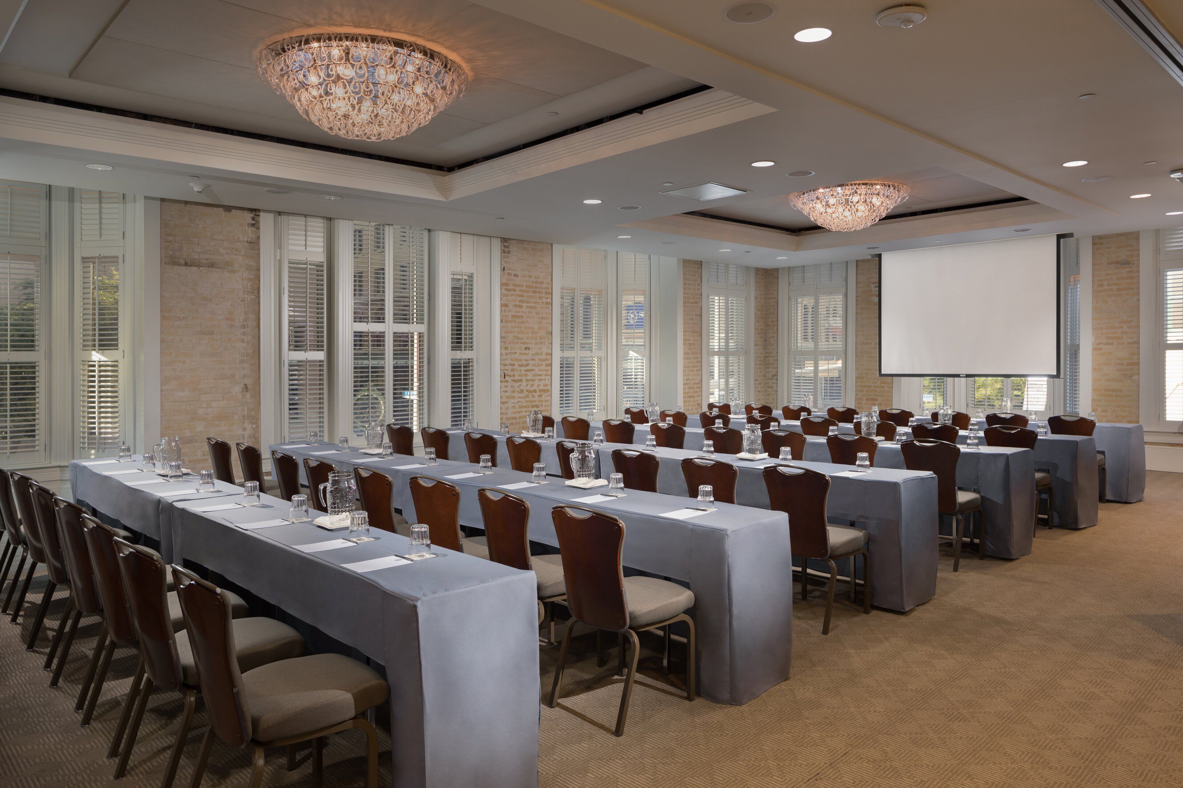 A conference room with long tables, chairs, and a projector screen.