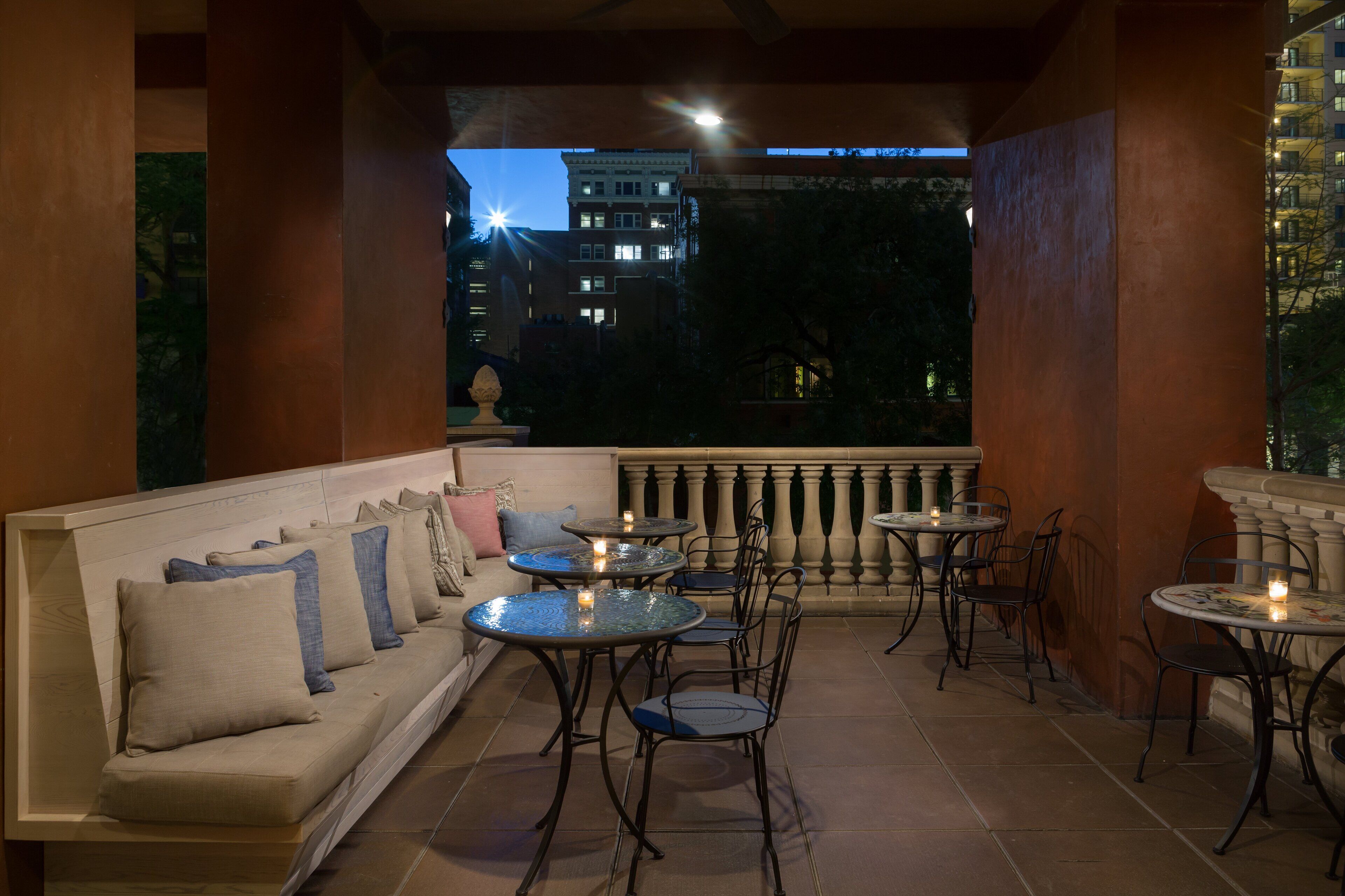Una terraza con sofá, sillas y mesas, que ofrece vistas de edificios al anochecer.