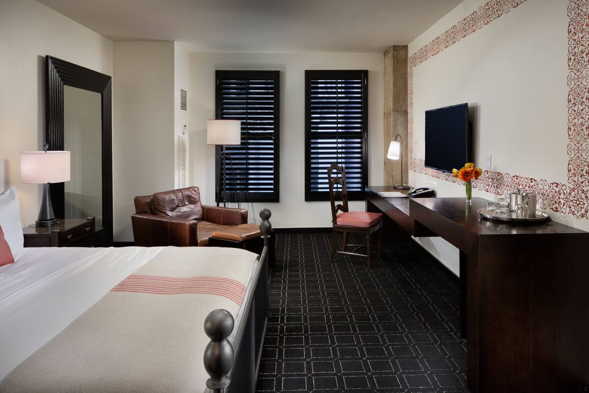 Een hotelkamer met een bed, een bureau, een stoel, een televisie en een raam met zonwering.