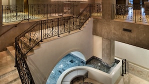 A grand staircase with ornate black railings, a marble floor, and a seating area with a patterned rug.