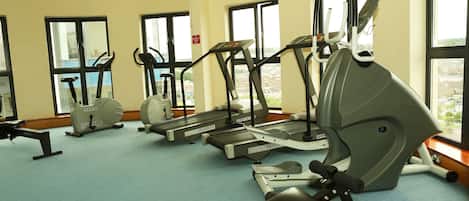 A gym with various cardio machines, large windows, and a view of the city.