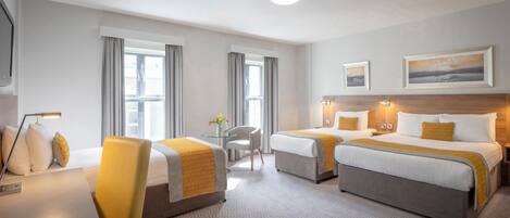 Une chambre d’hôtel avec deux lits, un bureau, une chaise et une petite table agrémentée de fleurs.