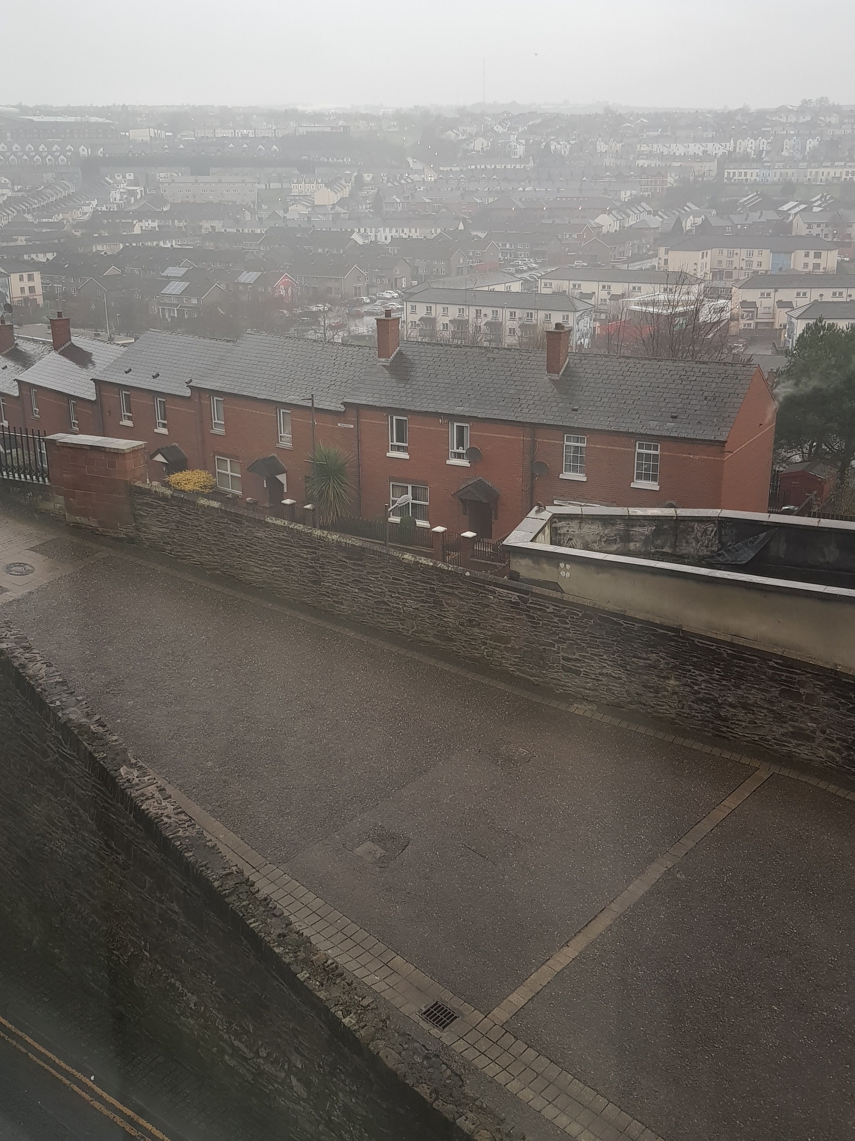 A residential area with terraced houses, a stone wall, and a paved road.