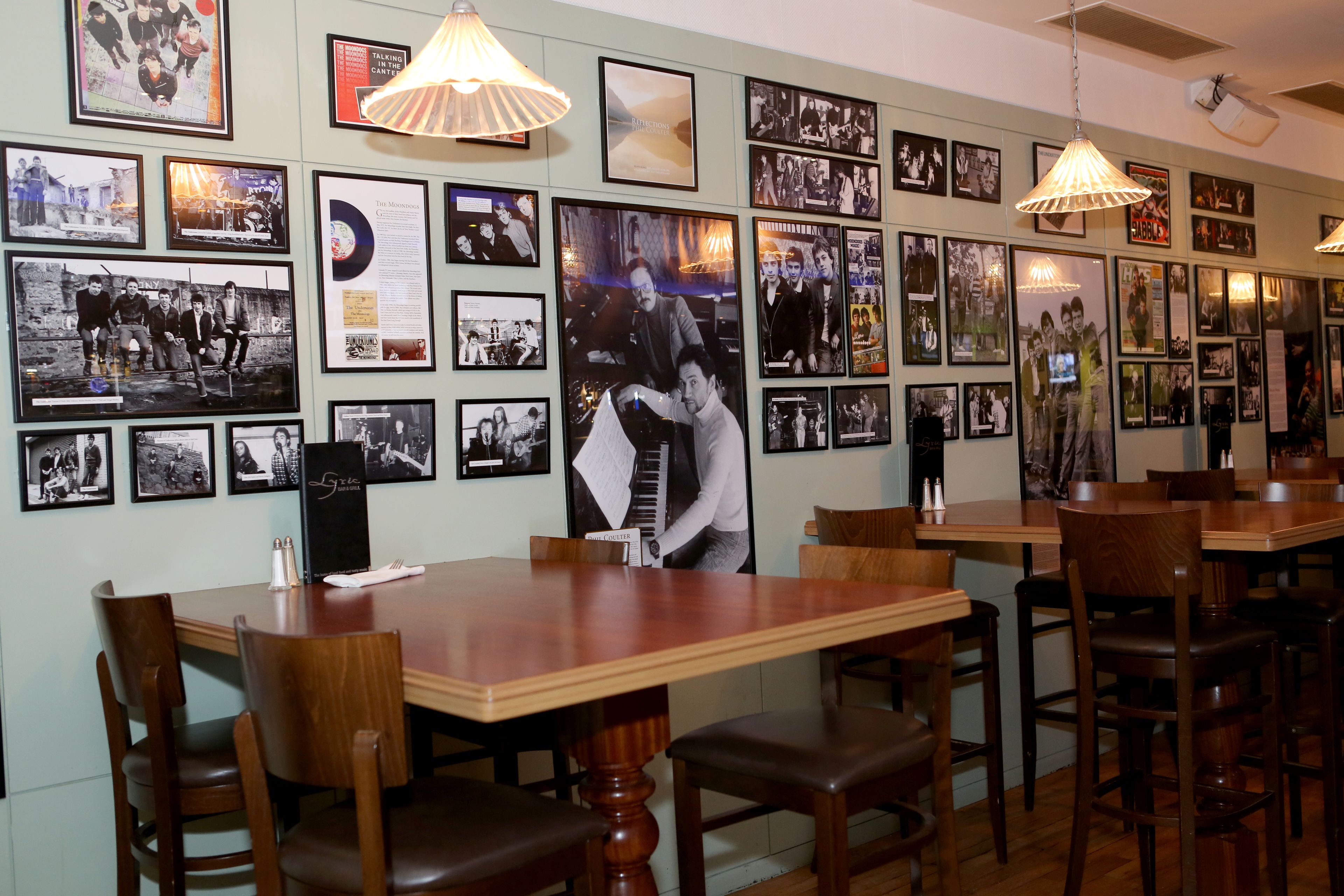 A restaurant with wooden tables and chairs, framed pictures on the walls, and pendant lights.