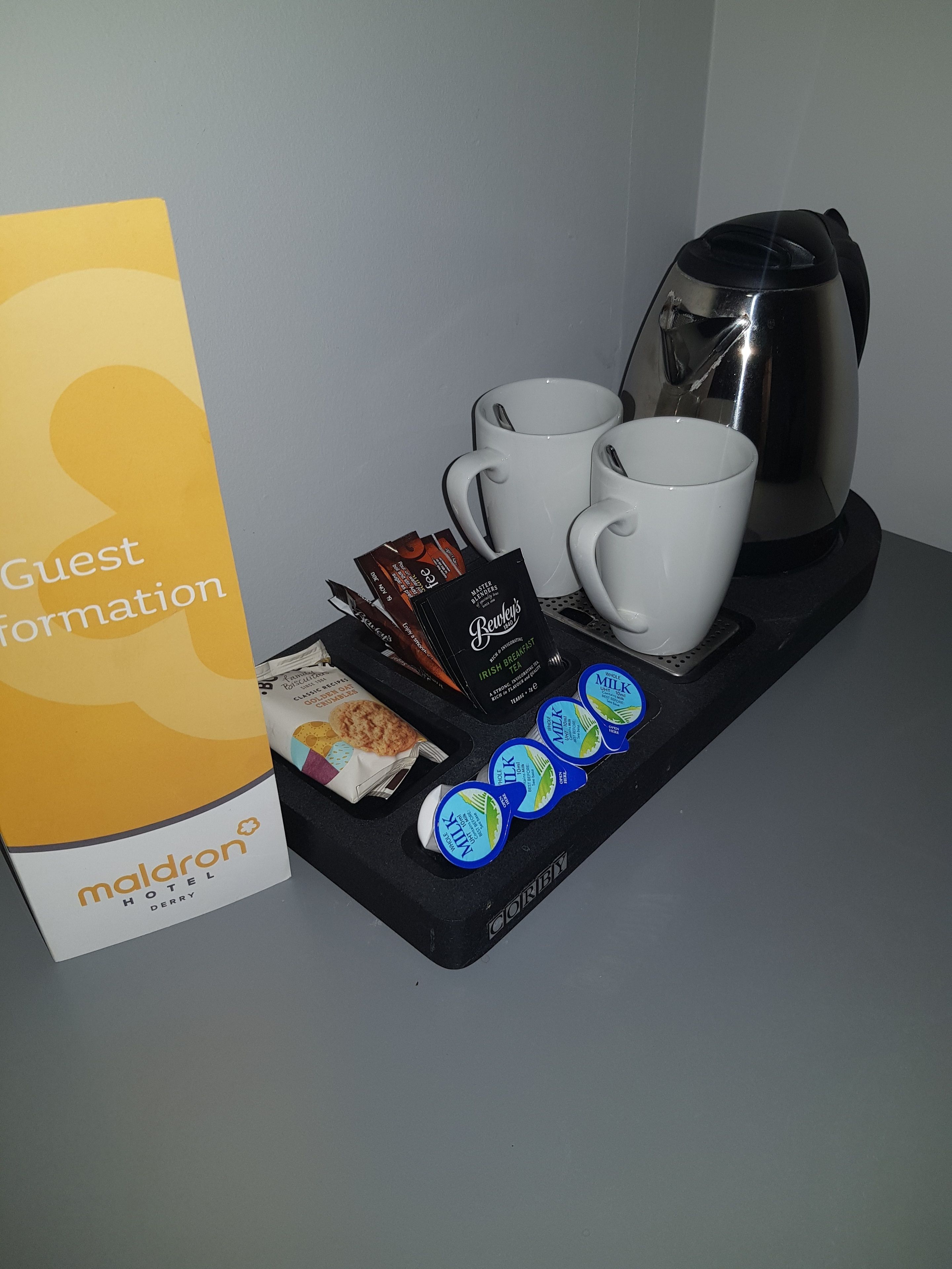 A tray with coffee pods, milk cartons, and two white mugs, alongside a sign for 'Maldron Hotel'.