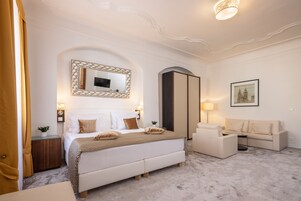Un dormitorio de hotel con una cama grande, una mesita de noche, un espejo, un armario, un sofá y una lámpara.