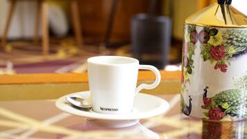 A white cup with a spoon on a saucer, a floral-patterned container, and a blurred background.