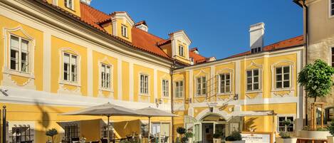 A courtyard with yellow buildings, outdoor seating, and potted plants.