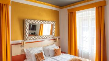 A hotel room with a bed, a bedside table, a mirror, and curtains.