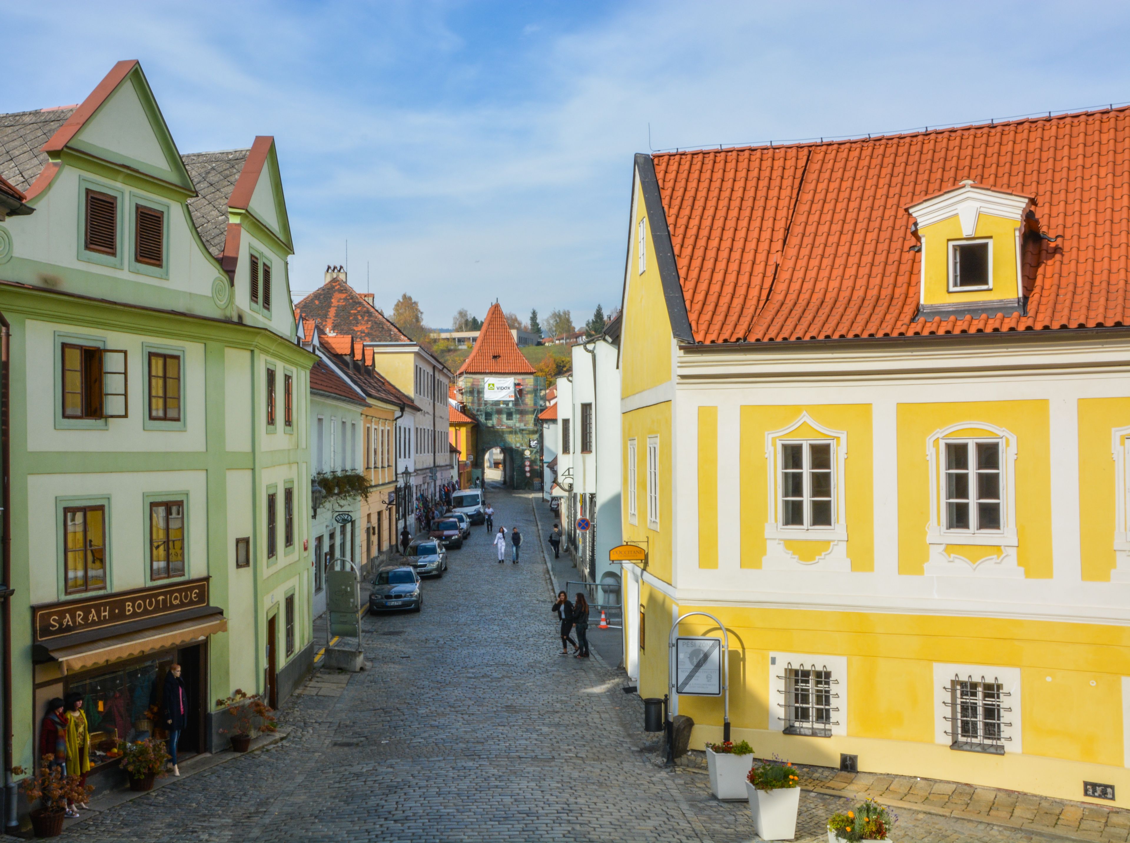 Une rue pavée bordée de bâtiments aux couleurs vives, dont une boutique et un bâtiment jaune avec un toit rouge.