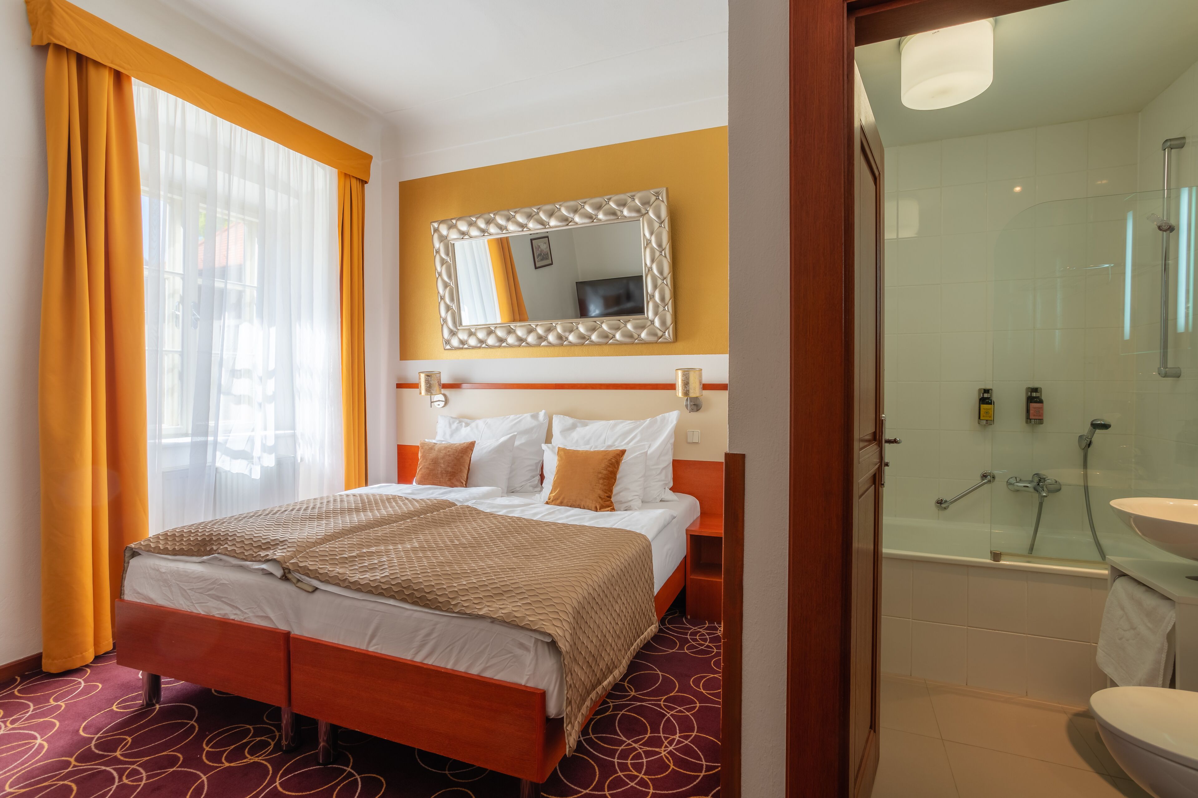 Habitación de hotel con cama, baño con bañera y un espejo grande en la pared.
