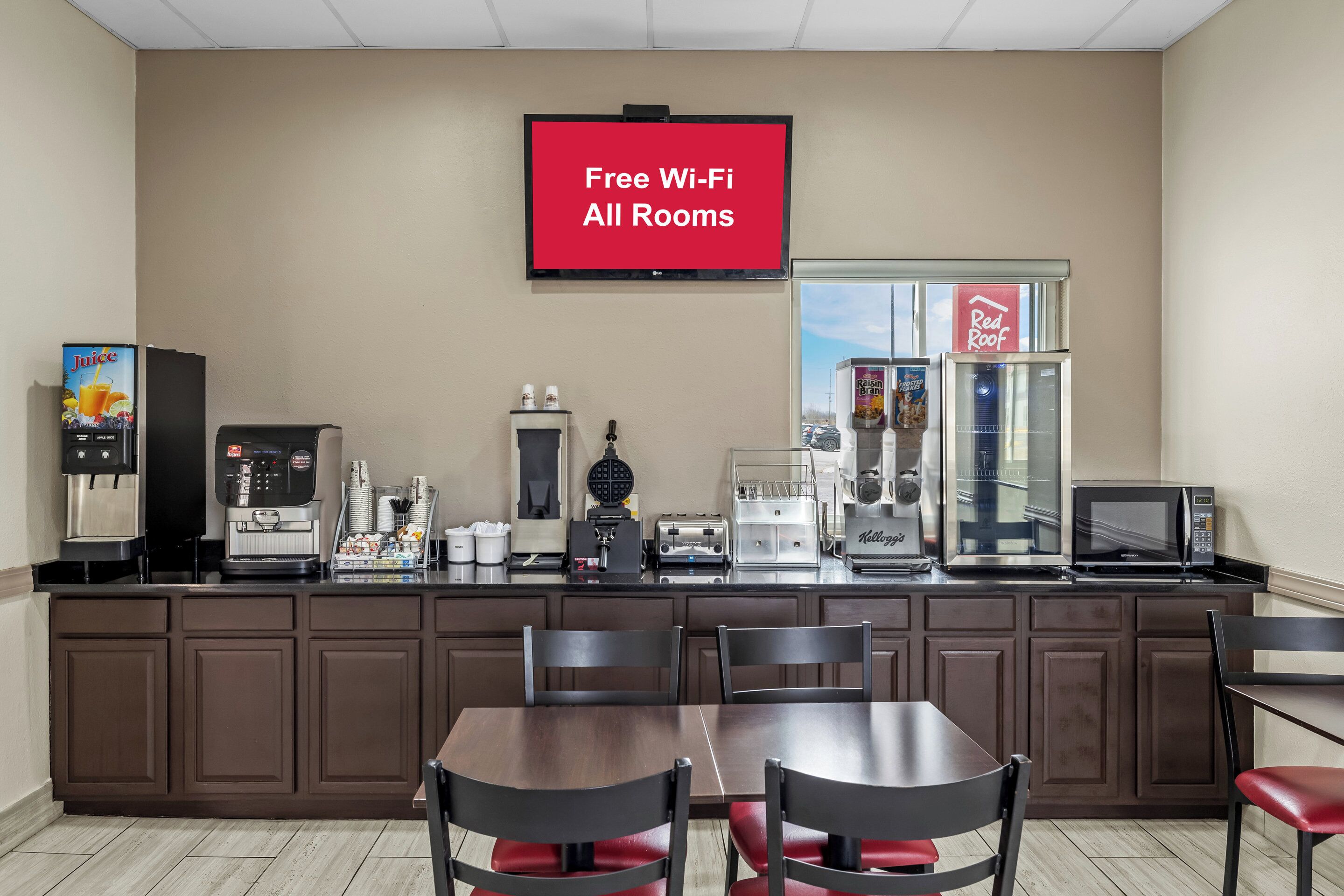 Eine Küchenzeile mit Kaffeemaschine, Toaster und Mikrowelle. An der Wand ist ein Fernseher installiert, der 'Kostenloses WLAN in allen Zimmern' anzeigt.