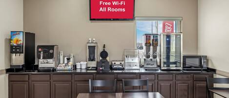 A kitchenette with a coffee machine, toaster, and microwave. There is a TV on the wall displaying "Free Wi-Fi All Rooms".