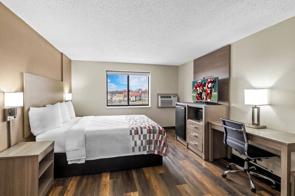 A hotel room with a bed, desk, chair, and a large window.