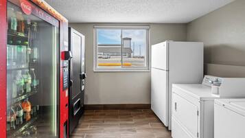 A compact kitchenette with a vending machine, a window with a view of a parking lot, and a refrigerator.