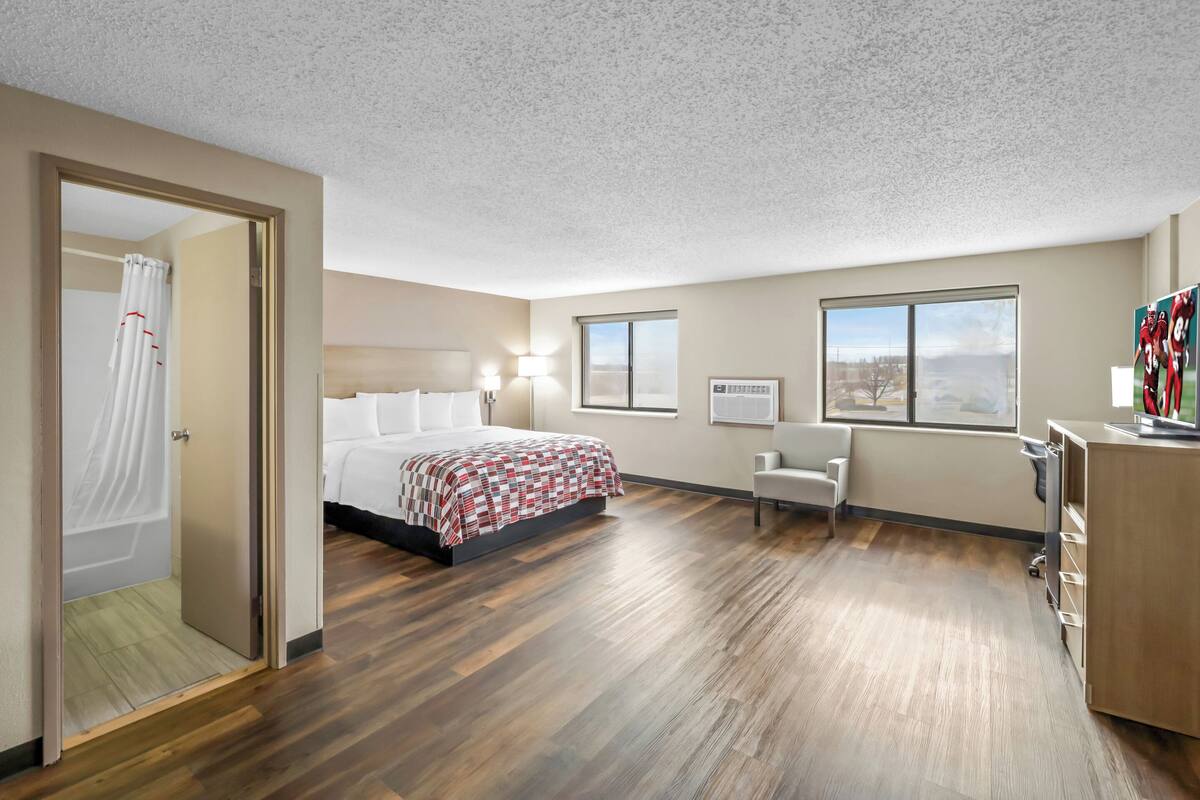 A hotel room with a bed, a desk, a chair, and a large window.