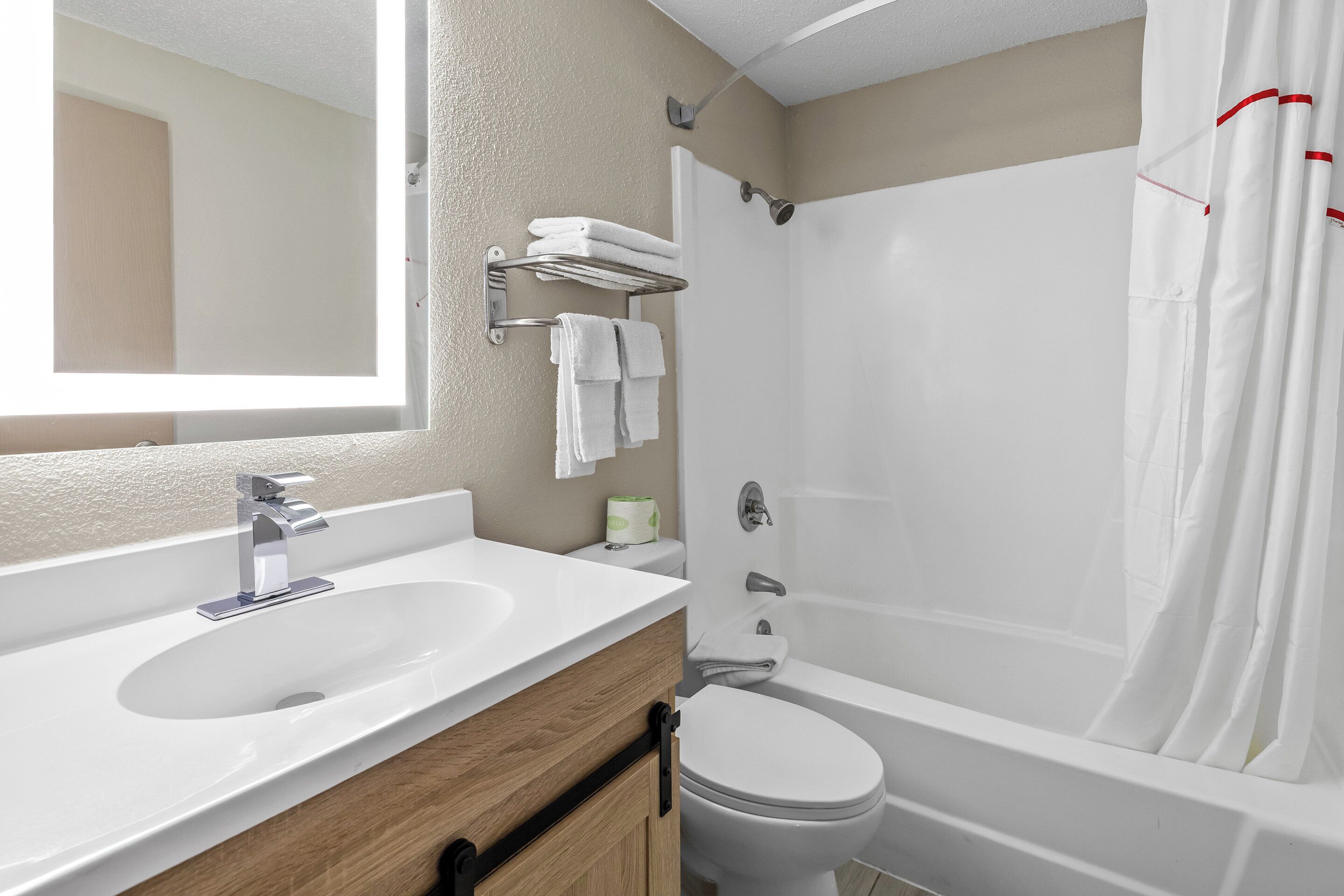 Un baño con lavamanos blanco, espejo, inodoro, cortina de ducha y toallero.