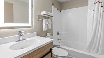 Un baño con lavamanos blanco, espejo, inodoro, cortina de ducha y toallero.