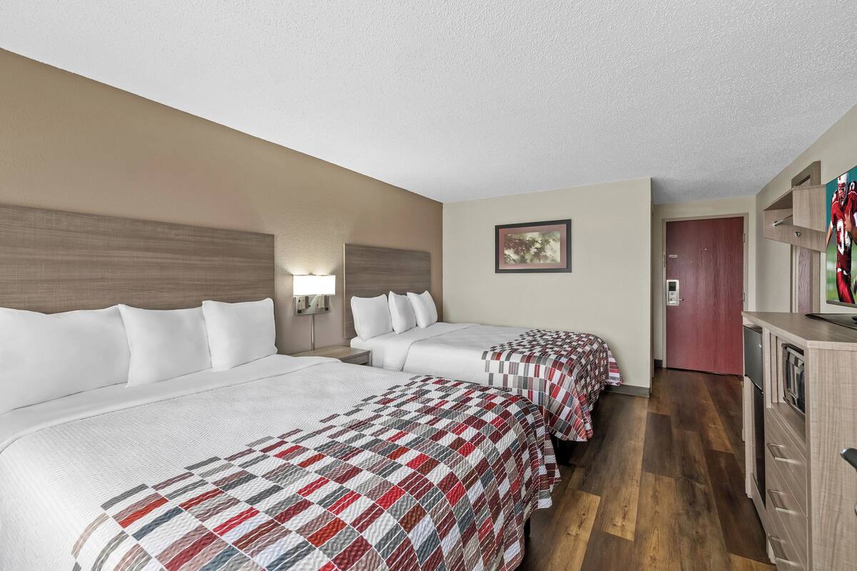 A hotel room with two beds, a desk, a dresser, and a painting on the wall.