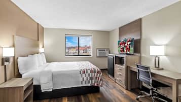 Una habitación de hotel con cama, escritorio, silla y un ventanal grande.