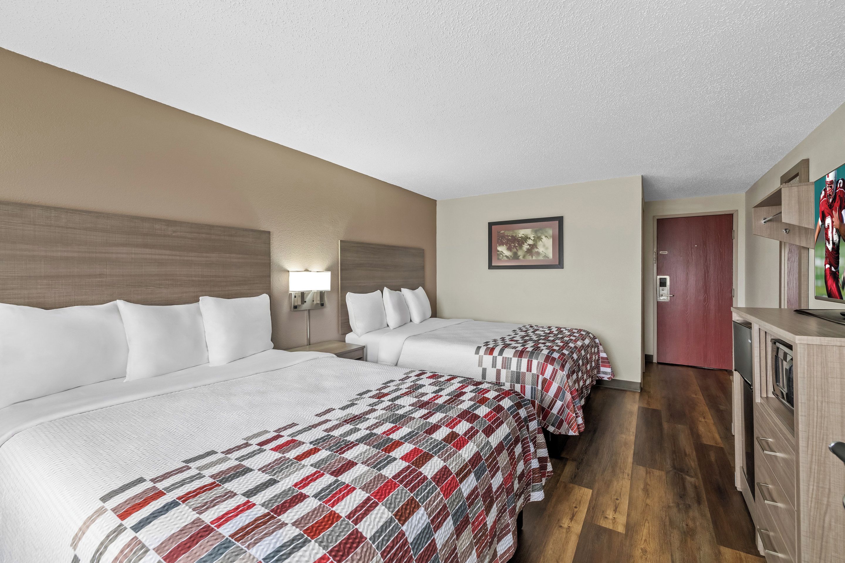 Una habitación de hotel con dos camas, un escritorio, una cómoda y un cuadro en la pared.