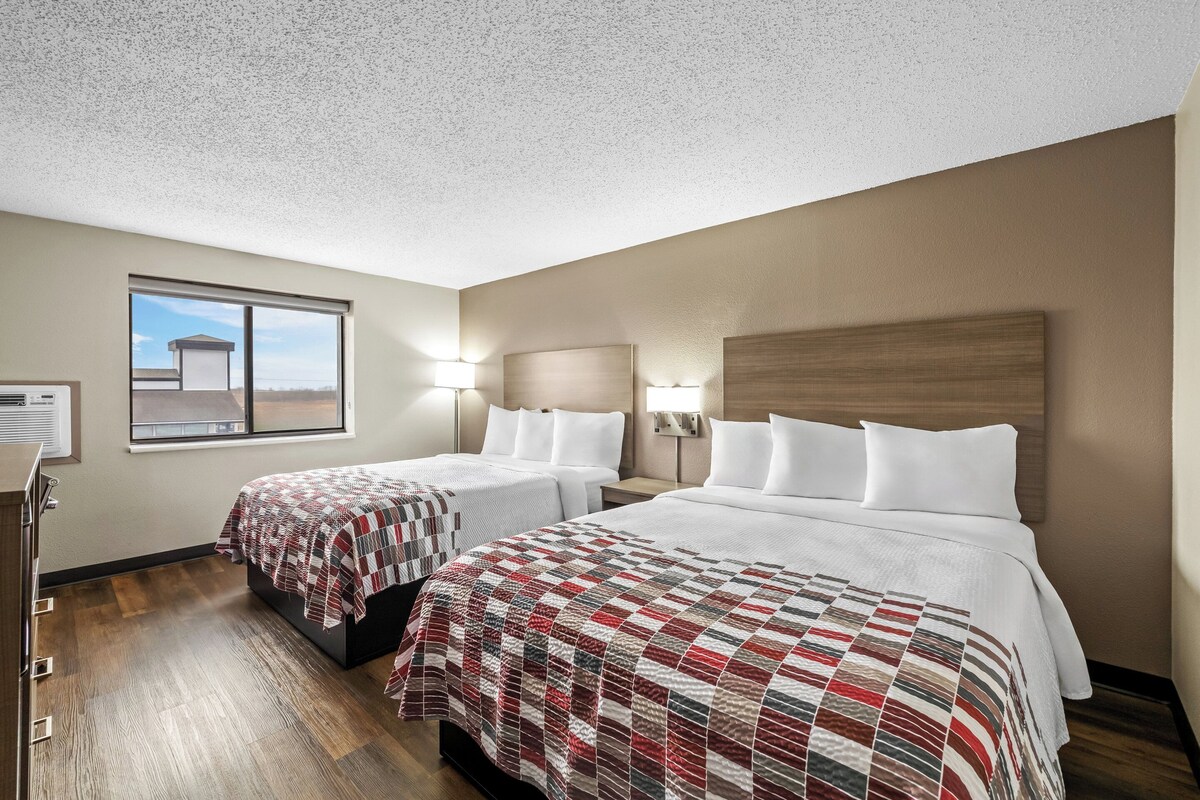 Ett hotellrum med två sängar, ett stort fönster och utsikt över en byggnad utanför.