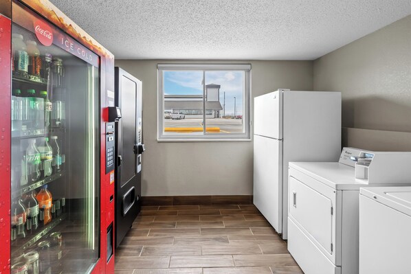 Una kitchenette compacta con una máquina expendedora, una ventana con vistas a un estacionamiento y un refrigerador.